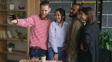 Selfie modern loft göreve mutlu çok etnik gruptan oluşan takım. Hipster adam holding smartphone almak meslektaşları ile kendi kendine portre