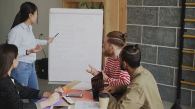 Başlangıç iş planı flipchart üzerinde modern loft ofiste iş arkadaşlarınıza açıklayan neşeli Asyalı kız