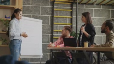 Başlangıç iş planı flipchart üzerinde modern loft ofiste iş arkadaşlarınıza açıklayan neşeli Asyalı kız