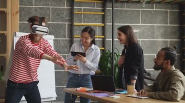 Modern ofisindeki VR oyun simülatörü test Mult etnik ekibi. Sanal gerçeklik kulaklık kullanarak sakallı hippi adam eğlenceli Asyalı kız kullanım oyun tablet ise hisseder