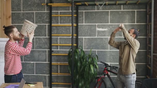 Двоє колег розважаються, граючи в баскетбол кидаючи папір у смітник в сучасному офісі — стокове відео