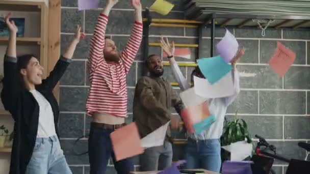 Různorodá skupina ženské a mužské start-up obchodní tým baví tanec strany v moderní kanceláři házení papírových dokumentů a slaví úspěch projektu — Stock video