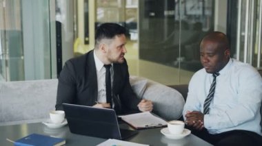 Siyah elbiseli kızgın işadamı onun Afro-Amerikan çalışan modern Café toplantı sırasında ağır eleştirdi. Tahriş olmuş patron duygusal gesticulates ve agresif Not