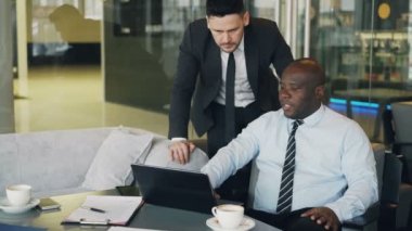Kendine güvenen modern kafe yakın duran Afrika CEO'su verir yönergeleri sakallı beyaz Yöneticisi iş için uygun. Afrika kökenli Amerikalı işadamı onun dizüstü bilgisayar işaret oturur