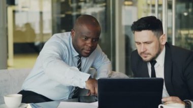 Dizüstü bilgisayar seyir ve cam duvarlı modern office projelerinde tartışırken iki iş arkadaşları. Sakallı işadamı ve masada oturan ve konuşurken ortağı