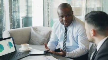 Grafikler ve diyagramlar dizüstü bilgisayarda bakarak ve mali yönleri başlangıç proje kafede kahve molası sırasında tartışırken Afrikalı Amerikan ve Kafkas işadamları