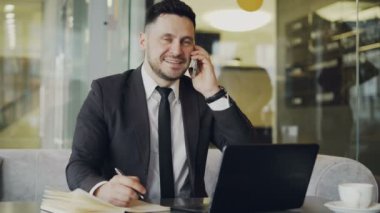 Gülümseyen ve cep telefonu üzerinde modern kafede konuşurken mutlu sakallı işadamı masada oturan siyah elbiseli