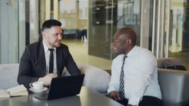 El sıkışan ve şık kafede başlangıç işlerini görüşmek üzere beyaz deri koltuklar koltuklarda alarak resmi giysili iki businessmaen
