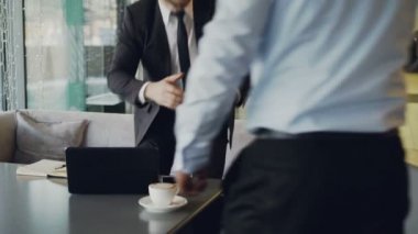 El sıkışan ve şık kafede başlangıç işlerini görüşmek üzere beyaz deri koltuklar koltuklarda alarak resmi giysili iki businessmaen