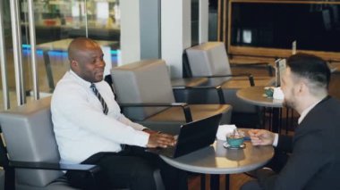 Resmi giyim gülümseyen iki çok ırklı işadamları, mimik ve onların başlangıç geniş kafede öğle yemeği sırasında tartışırken bölünürler. Onların gelişmiş dizüstü geçerli.