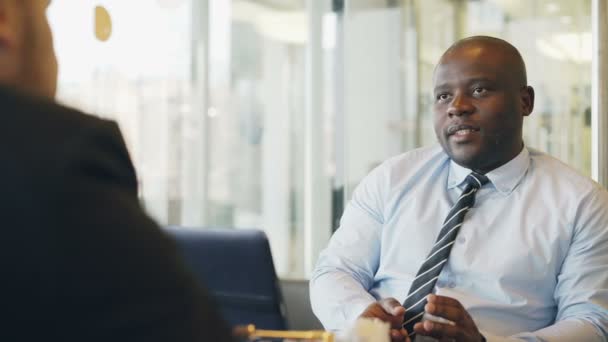 Hombre de negocios afroamericano gesticulando y explicando sus detalles de inicio a los inversionistas en ropa formal en un café vidrioso durante la hora del almuerzo — Vídeos de Stock