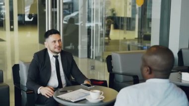 Neşeli beyaz işadamı resmi olarak Afrikalı-Amerikalı meslektaşı Cafe ile gülümseyen ve tartışırken iş kar giysiler. Genç garson kahve getiriyor.