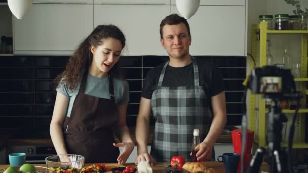 陽気な魅力的なカップルが自宅の台所でデジタル カメラのヘルシー クッキングについてビデオ食品ビデオブログを記録します。動画ブログやソーシャル メディアの概念 — ストック動画