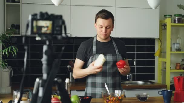 陽気な魅力的な男が自宅の台所でデジタル カメラのヘルシー クッキングについてビデオ食品ビデオブログを記録します。動画ブログやソーシャル メディアの概念 — ストック動画