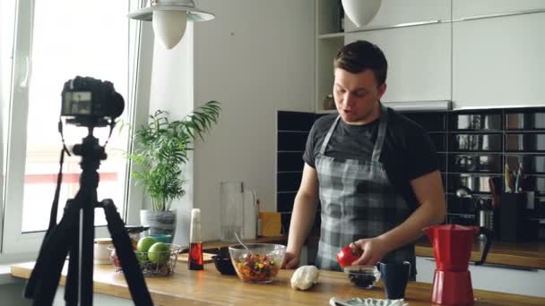 Yakışıklı adam evdeki mutfağın dijital kamerasında sağlıklı yemek pişirme hakkında video yemek bloğu kaydediyor. Vlog ve sosyal medya kavramı — Stok video
