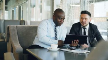 Neşeli Afrikalı-Amerikalı iş adamı resmi kıyafet öğle yemeği molası sırasında beyaz onun ortağı bulunan şık kafe başlangıç projesi tartışmaya dijital tablet kullanma
