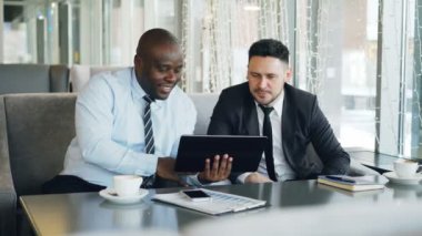Neşeli Afrikalı-Amerikalı iş adamı resmi kıyafet öğle yemeği molası sırasında beyaz onun ortağı bulunan şık kafe başlangıç fikirler tartışırken dijital tablet kullanma