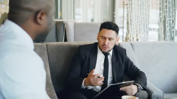 Empresário caucasiano feliz rindo, gesticulando e discutindo seu projeto de startup com parceiro de negócios enquanto bebe café no café — Vídeo de Stock