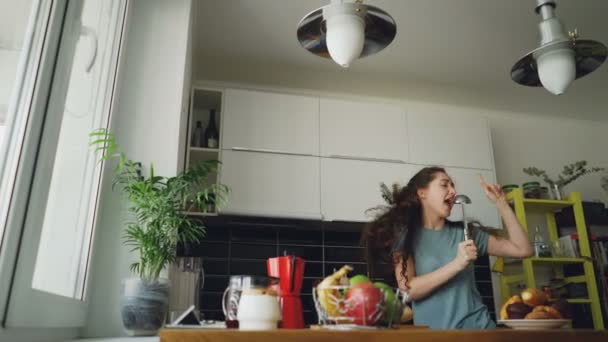 Jovem alegre mulher engraçada dançando e cantando com concha enquanto tem tempo de lazer na cozinha em casa — Vídeo de Stock