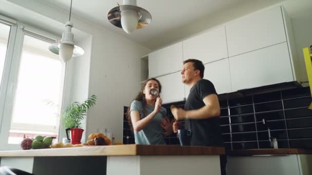 Genç neşeli çift dans eğlenceli ve tatillerde evde mutfakta kahvaltı sırasında şarkı var. — Stok video