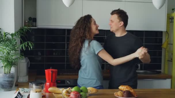 Aantrekkelijke jonge vrolijke paar veel plezier dansen tijdens het koken in de keuken thuis — Stockvideo