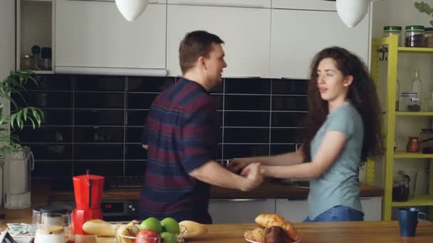 Привлекательная молодая радостная пара веселятся танцы во время приготовления пищи на кухне дома — стоковое видео