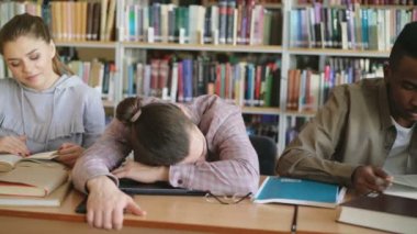 Çalışkan öğrenciler ödev ve yorgun adam üniversite kitaplığında masada uyku yapıyor sınavlarına hazırlanıyor kadeh kaydırmak