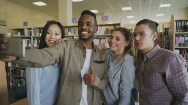 Grup uluslararası öğrenci eğlenceli gülümseyen ve akıllı telefon kamera Üniversitesi Kütüphanesi'nde selfie fotoğrafları yapma. Neşeli arkadaşları birlikte preapre proje sırasında dinlenme hakkına sahiptir