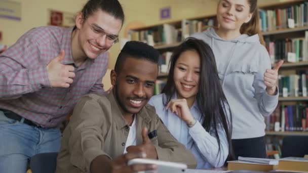 Skupina zahraničních studentů bavte se usmívá a fotí selfie na fotoaparát smartphonu v univerzitní knihovně. Veselí přátelé mají odpočinku při preapre projektu společně — Stock video