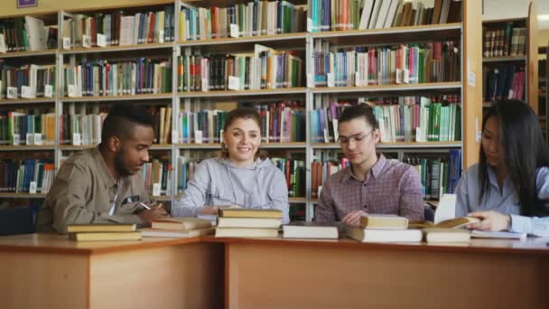 Multi εθνοτική ομάδα φοιτητών κουβεντιάζοντας και προετοιμασία για εξετάσεις, ενώ κάθεται στο τραπέζι στη βιβλιοθήκη του Πανεπιστημίου — Αρχείο Βίντεο