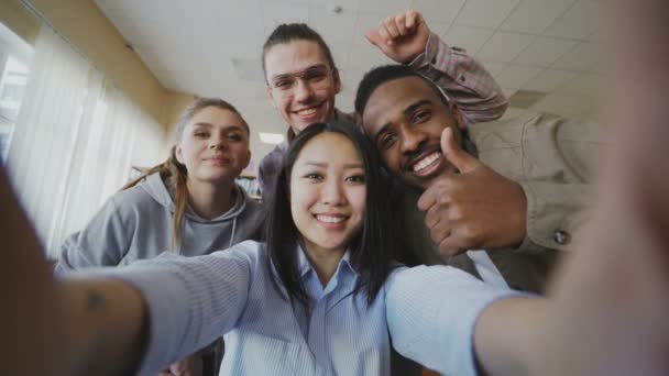 POV de chica asiática sosteniendo teléfono inteligente tomando fotos selfie con compañeros de clase multiétnicos alegres y divertirse en la biblioteca de la universidad. Mujer señalando touchsreen y viendo fotos — Vídeos de Stock