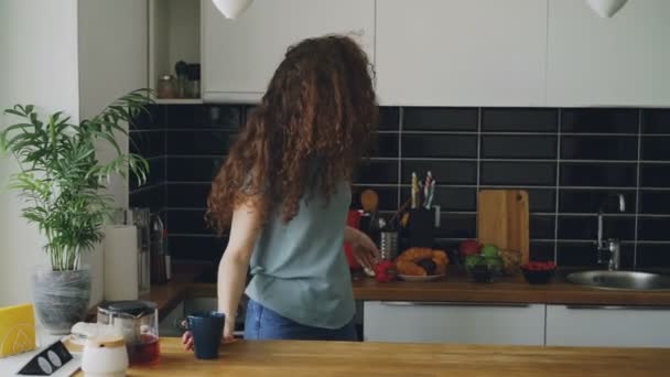 Joven hermosa rizado caucásico mujer bailando poner croissants en mesa su novio viene y ayuda, agradable pareja sirve mesa con verduras juntos — Vídeo de stock