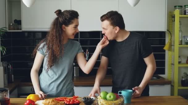 Positieve jonge Kaukasische paar luisteren naar muziek op smartphone dansen, vrouw snijden rode peper en geven om te proberen haar echtgenoot, dan geeft man haar om te proberen een stukje peper — Stockvideo