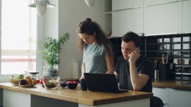 ciddi çift mutfak, kadın salata kesme, sessiz duruyor, adam üstünde laptop çalışma masasında oturuyor ve telefonda konuşurken, o rahatsız