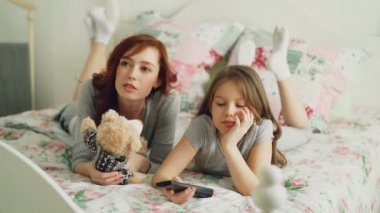 Neşeli mutlu anne ile Tv kullanma sevimli çizgi film film izlerken uzaktan ve gülümseyerek evde yatakta sabah rahat yatak odasında yatarken
