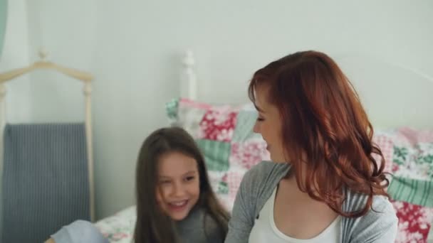 Pequeña linda chica dando caja de regalo a su joven madre feliz celebrando el día de las madres sentadas en la cama en el acogedor dormitorio en casa — Vídeo de stock