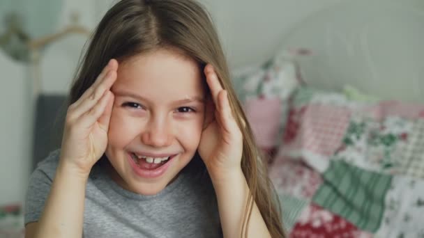 Close-up de bonito menina engraçada cobre seu rosto e mãos abertas sorrindo e sorrindo olhando para a câmera sentada no quarto em casa — Vídeo de Stock