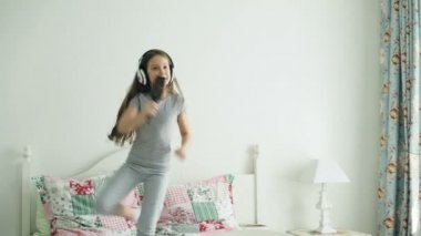 Sevimli küçük kız dans kablosuz kulaklık ile şarkı tarak ve eğlenceli tatil sabah evde yatakta ışık yatak üzerinde atlama