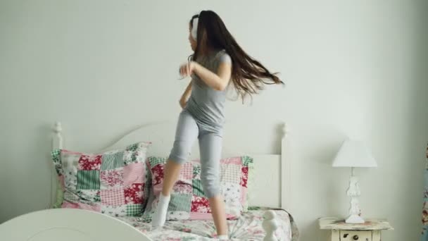 Funny roztomilé děvčátko v bezdrátových sluchátek tančit a bavit se na posteli doma v útulnou ložnici — Stock video
