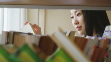 Çekici Asya öğrenci kız Üniversite Kütüphanesi kitap okuma sayfaları çevirme kitaplarda ile raf yakınındaki ayakta
