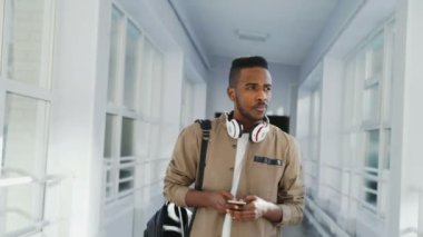 Düşünceli telefon gülümseyen ve beyaz ve Asyalı kızlar pencere daimi için el sallayarak holding univrsity koridorda yürürken yakışıklı afro öğrenci