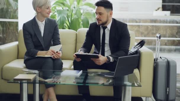 Two female and male business colleagues with clipboard and notepad talking at hotel lobby. Luggage in near couch. Business, travel and people concept — Stock Video