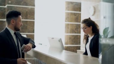 Otel Resepsiyon masasında duran ve temassız ödeme teknolojisi üzerinden kredi kartı ile fatura ödeme resepsiyonist kızla konuşan işadamı konuk. İş, seyahat ve insanlar kavramı