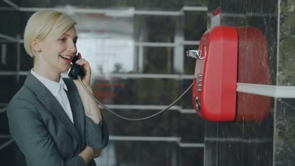 Vrolijke zakenvrouw in gesprek met medewerkers met bekabelde rode telaphone bij de receptie in de lobby van het hotel. Business, reizen en mensen concept — Stockvideo