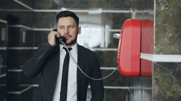 Homme d'affaires barbu composer téléphone rouge parler avec le personnel de la réception dans le hall de l'hôtel. Concept affaires, voyages et personnes — Video