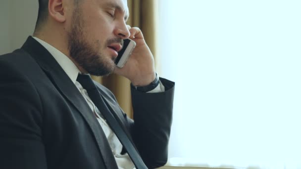 Närbild nedtiltning säker affärsman prata mobiltelefon och skriva anteckningar i anteckningar medan du sitter på fåtölj i hotellrum eller office. Resor, affärer och människor-konceptet — Stockvideo
