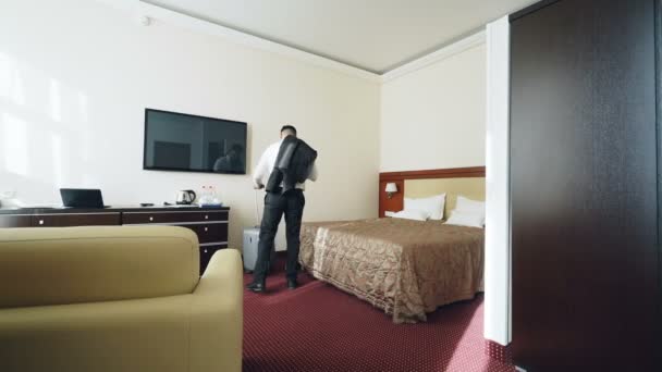 Empresario con equipaje entrando en la habitación del hotel y saltando en la cama felizmente luego acostado relajado sonriendo. Concepto de viajes, negocios y personas — Vídeo de stock