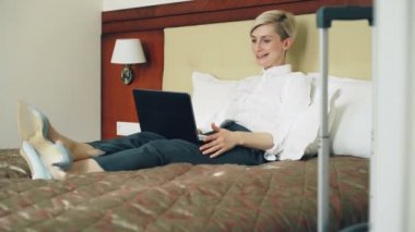 Mutlu işkadını otel odasında yatakta yatan dizüstü bilgisayar kullanan online video sohbet yoluyla ailesiyle konuşuyor. Seyahat, iş ve insan kavramı