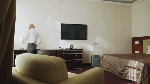 自信的女商人在酒店房间里走动时用手机交谈。旅游, 商业和人的概念 — 图库视频影像
