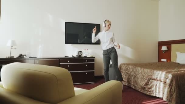 Bizneswoman szczęśliwy taniec i śpiew podczas słuchania muzyki na bezprzewodowe słuchawki podczas zabawy, spacery w pokoju hotelowym. Koncepcja podróży, firm i osób — Wideo stockowe